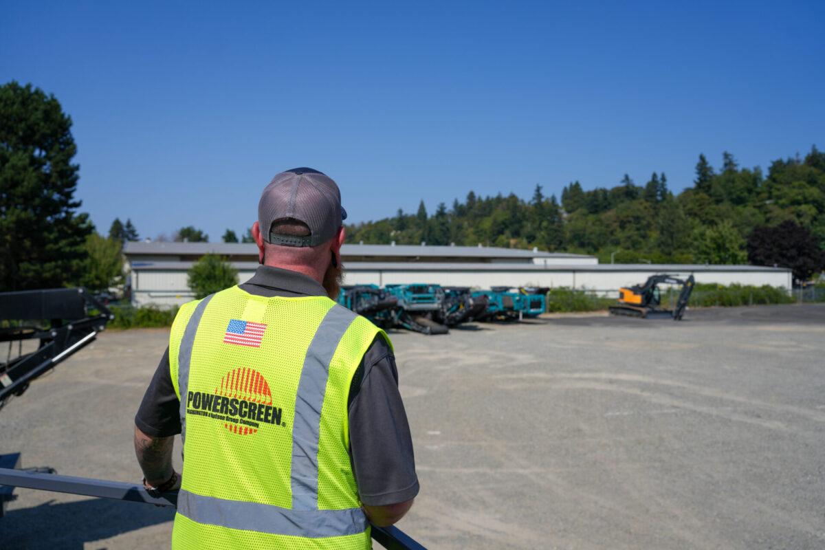 Man overlooking Powerscreen machines in a yard wearing a hi-vis vest