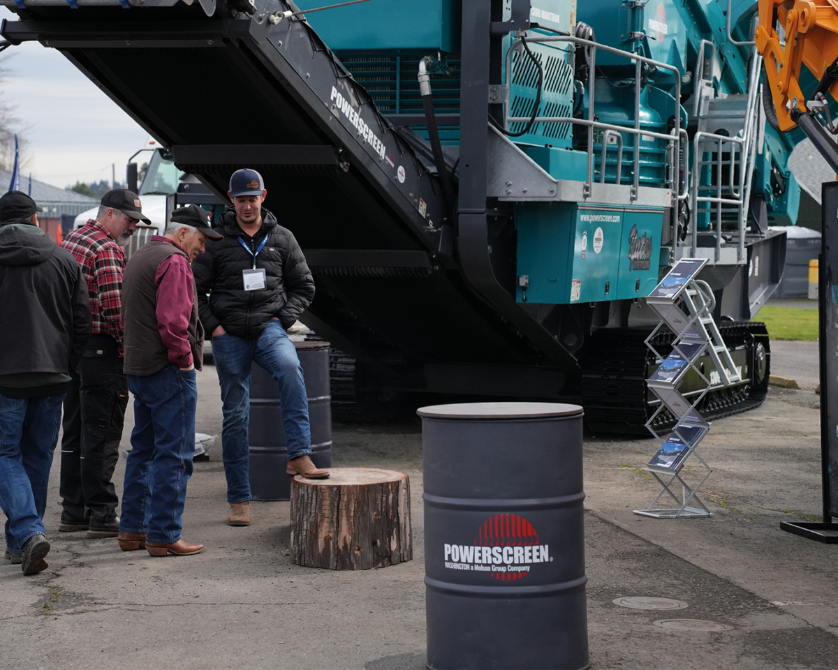 Barrel drum with Powerscreen of Washington logo and men looking at a log