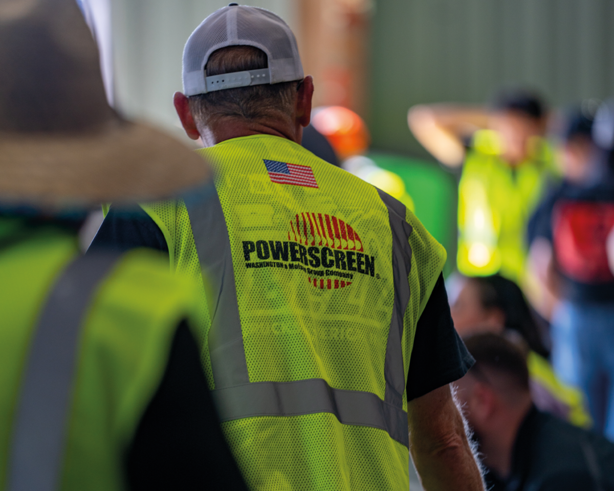 The back of a man wearing a safety hi-vis vest with the Powerscreen of Washington logo